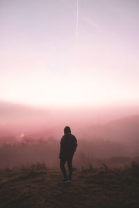 Rear view of person standing on field during foggy weather