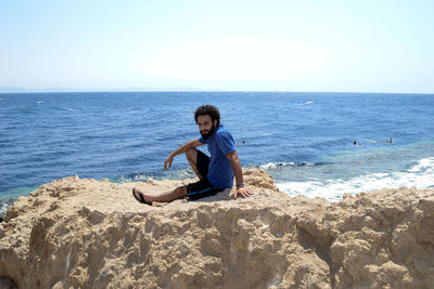 Portrait of man sitting on rock at beach against sky