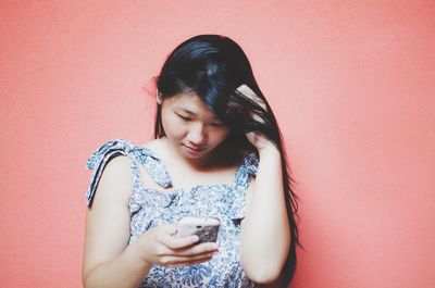 Young woman using mobile phone against red background