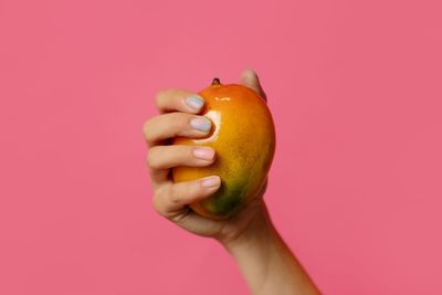 Close-up of hand holding apple against pink background
