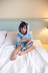Baby boy two years old in a blue terry robe with a hood lying on a big bed