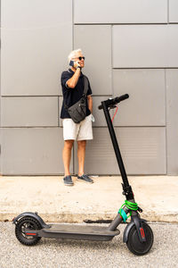 Commuter hipster man with electric scooter using smartphone in the suburbs. eco transport concept 