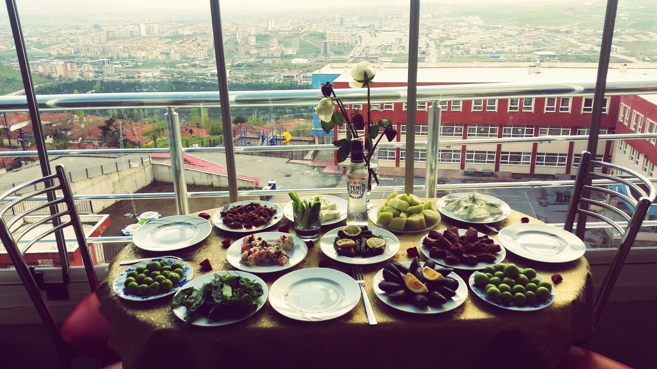 food and drink, table, freshness, city, restaurant, food, architecture, building exterior, built structure, glass - material, incidental people, chair, day, indoors, potted plant, plate, drink, cafe, window