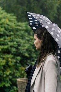 Rear view of woman with umbrella standing against trees