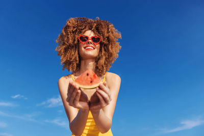 Low angle view of young woman standing against blue sky