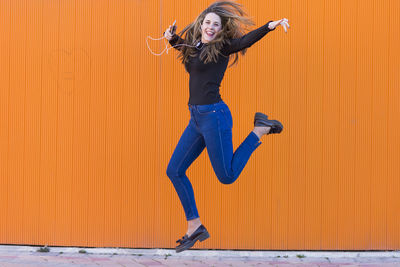 Portrait of young woman jumping against orange wall
