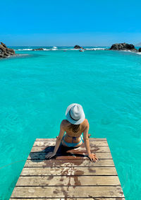 Rear view of woman sitting on pier over sea against sky