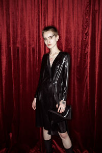 Portrait of young woman standing against red curtain