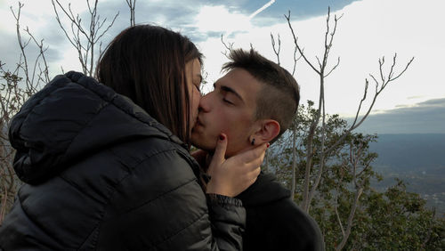 Close-up of young couple kissing against sky