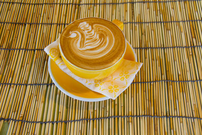 High angle view of cappuccino served in cup on straw mat