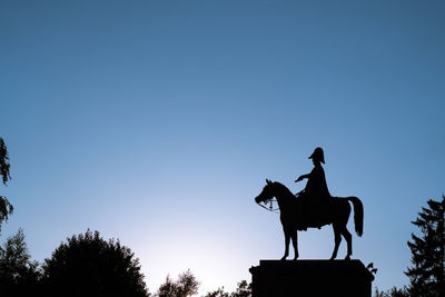 Low angle view of silhouette statue against clear blue sky