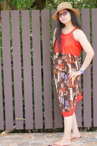 Portrait of young woman wearing hat while standing against fence