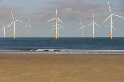 Wind turbines on beach against sky