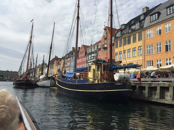 Sailboats moored on canal in city against sky