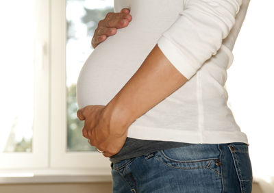 Midsection of pregnant woman with hands on abdomen at home