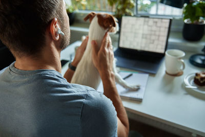 Man sitting at table by the window with dog and using laptop