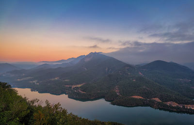 Scenic view of lake and mountains against sky at sunset