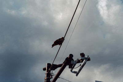 Low angle view of people sitting on pole against sky