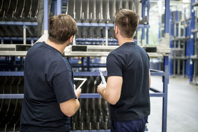 Two workers with clipboard and tablet in factory warehouse