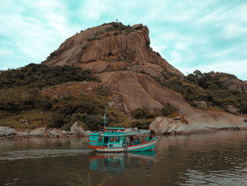 Boat moored on sea by rock formation against sky
