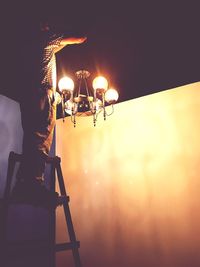 Low angle view of man photographing illuminated lamp against sky