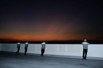 Rear view of people standing by sea against sky during sunset