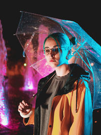 Young woman wearing sunglasses standing against illuminated wall at night