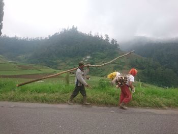 People walking on road by mountain against sky