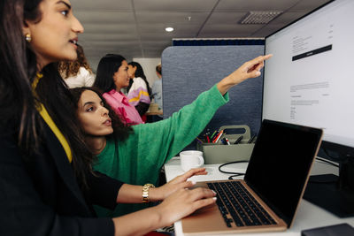 Businesswoman pointing at monitor screen with colleague working on laptop at office