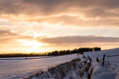 Snow covered field against sky during sunset