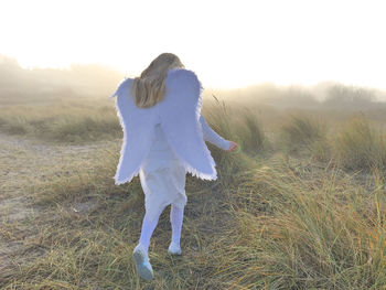 Rear view of girl wearing angel costume while running at beach during foggy weather