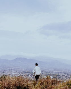 Rear view of man walking on mountain against sky