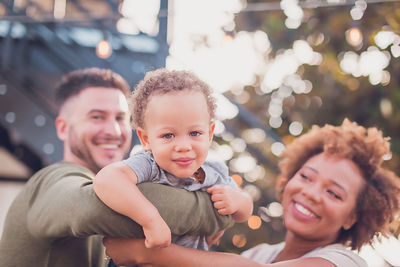 Black mom and white dad holding baby boy and playing airplane