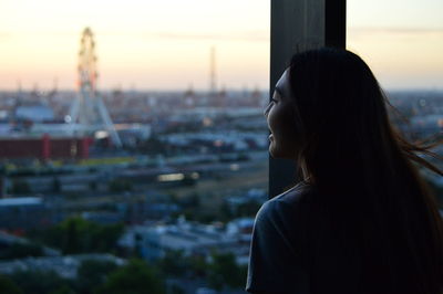 Rear view of smiling young woman looking through window at sunset