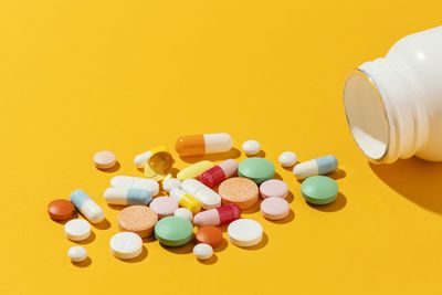 Pills spilling from bottle against yellow background