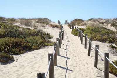 Railing on pathway at beach against clear sky on sunny day