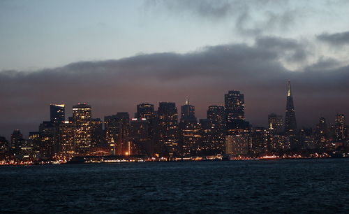 Illuminated buildings in city against sky at dusk