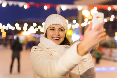 Portrait of smiling young woman standing against illuminated during winter