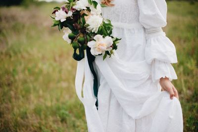 Midsection of bride holding flowers while standing on field