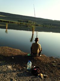 Rear view full length of man fishing by calm lake
