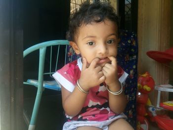 Portrait of girl with fingers in mouth sitting at home