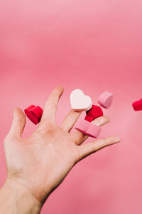 Close-up of hand holding pink flower over colored background