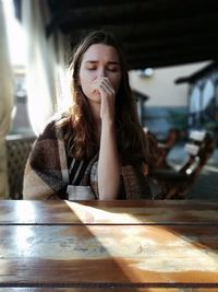 Thoughtful woman with closed eyes wrapped in blanket sitting at restaurant