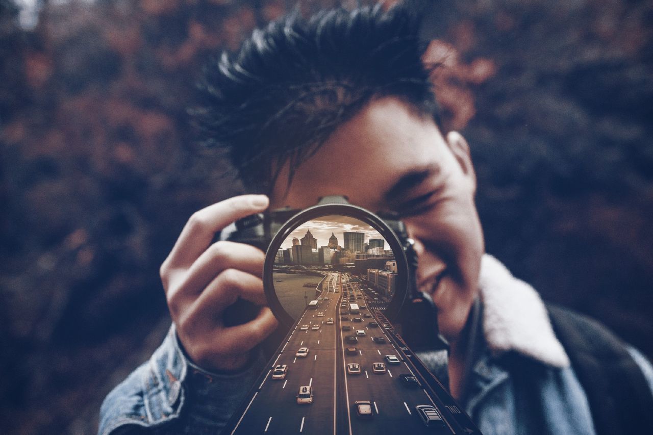 PORTRAIT OF MAN HOLDING CAMERA OUTDOORS