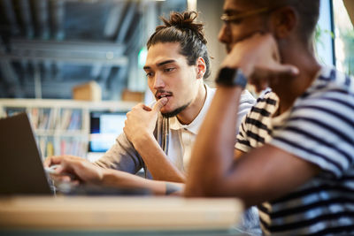 Male entrepreneurs discussing over laptop at desk in creative office