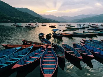 Rowboats moored on lake against sky during sunset