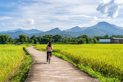 Rear view of woman walking on field against sky