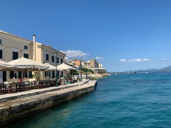 Buildings by sea against blue sky