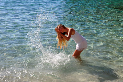 Side view of young woman splashing water in sea in minorca island