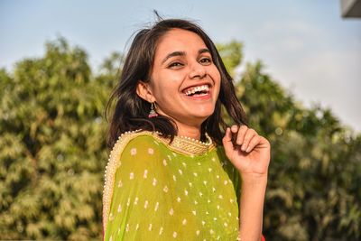 Portrait of smiling young woman standing against trees